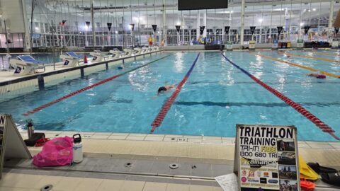 Indoor pool with swimmers, triathlon training signage, and lane dividers.