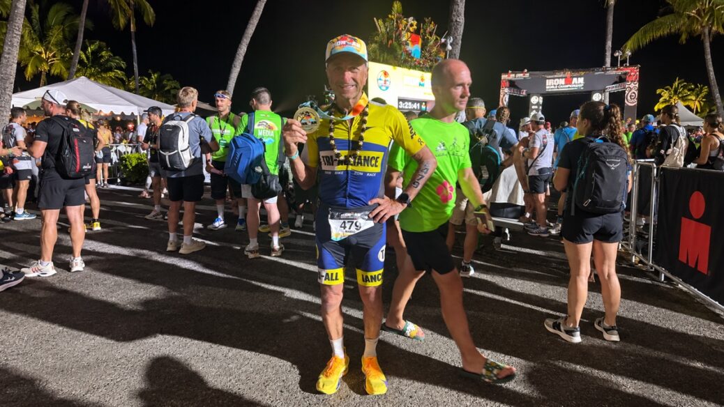 Male triathlete holding finish medal at night Ironman event.