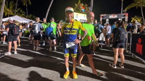 Male triathlete holding finish medal at night Ironman event.