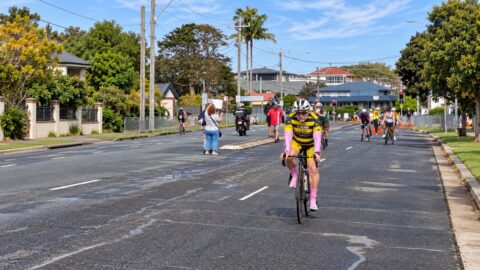 Cyclists riding bikes in a street event with spectators and palm trees